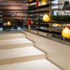 Interior con estantes de madera, lámparas y escalones en Neolith Arena beige, ambiente contemporáneo.