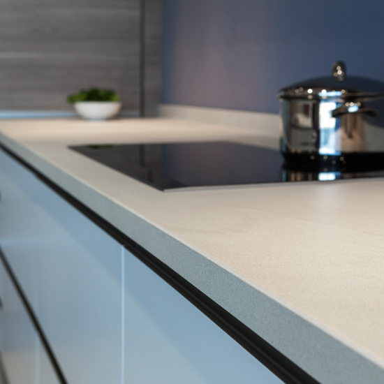 Close-up de encimera Neolith Arena con placa inducción negra, olla y gabinetes azules.