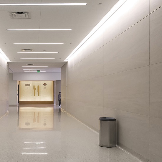 Pasillo largo con paredes y suelo en Neolith Arena beige, iluminación lineal y persona al fondo.