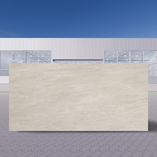 Losa grande de Neolith Arena beige en entorno exterior industrial, bajo cielo azul.
