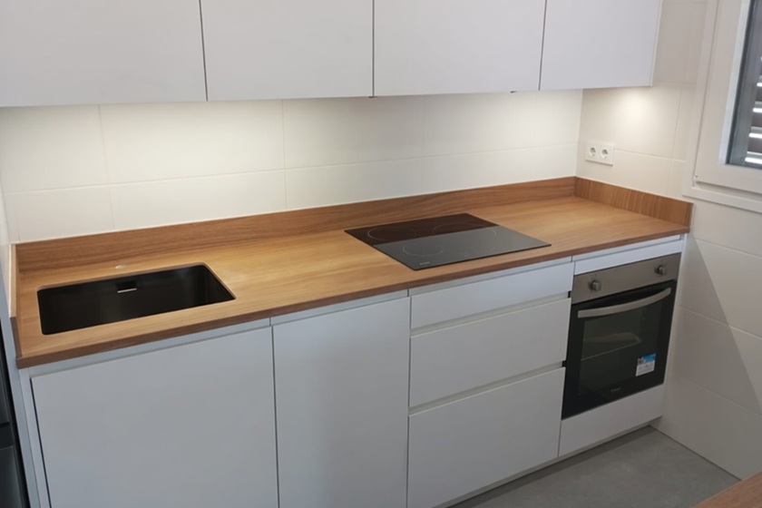 Instalación profesional de encimera porcelánica efecto madera Xtone E Wood Camel en cocina moderna de piso en Málaga ciudad 2025 con canto inglete 4 cm, fregadero negro y placa inducción. Tonos camel cálidos naturales y textura realista.