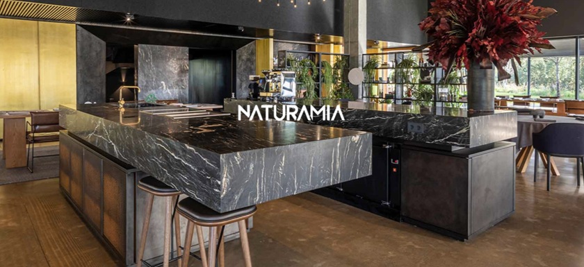 Encimera Naturamia en un bar moderno y elegante: superficie negra exótica con vetas blancas dramáticas, rodeada de plantas y asientos, destacando durabilidad y diseño premium para reformas en Málaga.