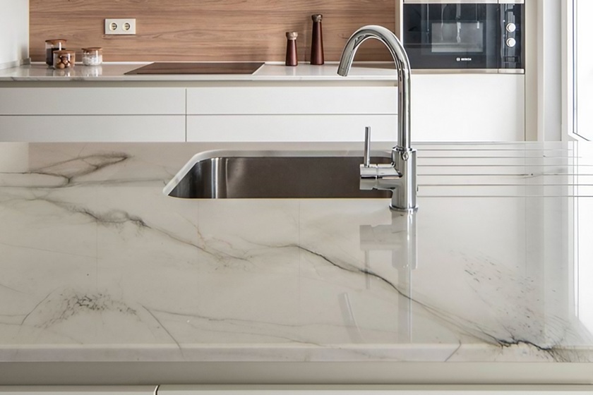 Encimera de cuarcita Naturamia Calacatta Boheme en cocina minimalista, con vetas neutras en blanco cremoso, negro profundo y óxidos, resistente y trendy para reformas de alta gama.