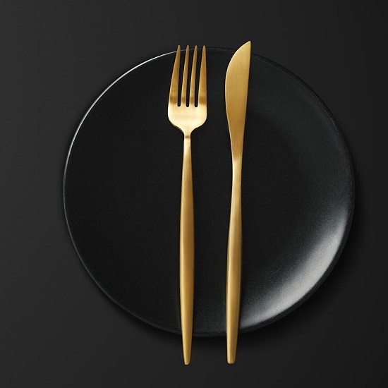 Encimera Arklam Pure Black negra decorada con plato y cubiertos dorados para cocinas en Málaga.