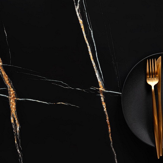 Encimera Arklam Sahara Noir negra con vetas doradas, decorada con plato y cubiertos para cocinas en Málaga.