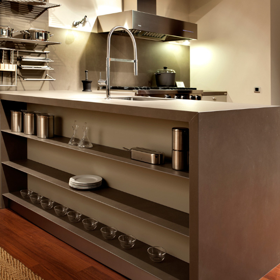 Isla de cocina Neolith Barro terracota con estantes, frascos y utensilios en entorno luminoso.