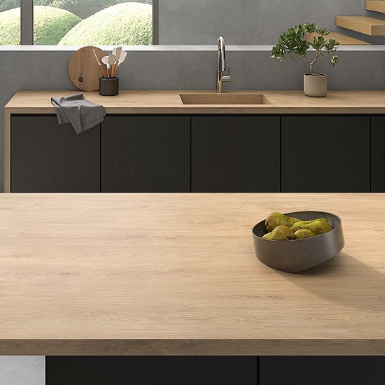 Encimera Arklam Arcane Camel madera con bol de peras, fregadero y gabinetes negros en cocina moderna.