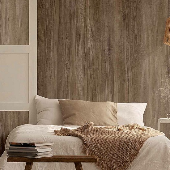 Dormitorio con pared Arklam Canada madera marrón, cama blanca con manta y libros en mesita.