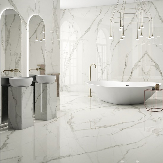 Baño de lujo con revestimientos y encimeras Arklam Estatuario en Málaga, bañera blanca y grifería dorada.