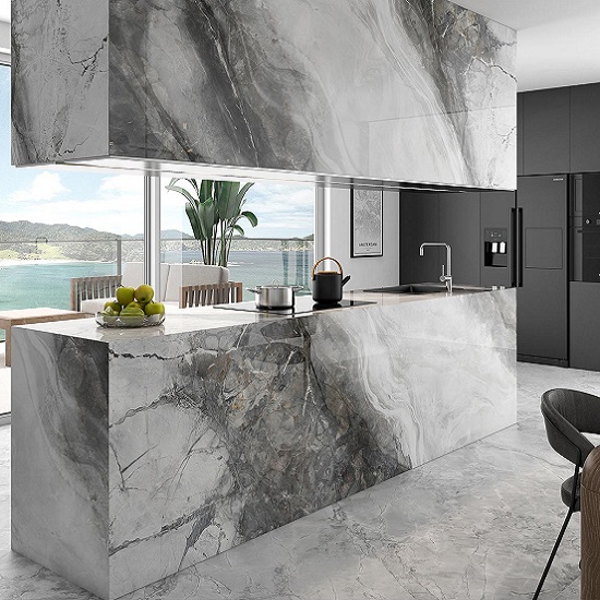 Cocina moderna con isla Arklam Invisible Grey gris veteada, gabinetes negros, fruta y vista oceánica.