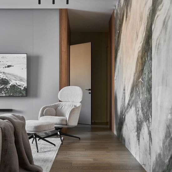 Vista lateral de sala con pared Arklam Invisible Grey veteada, sillón blanco, TV y suelo de madera.