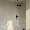Revestimiento Dekton Nara en ducha moderna con paredes y suelo beige, ducha negra y bañera blanca.