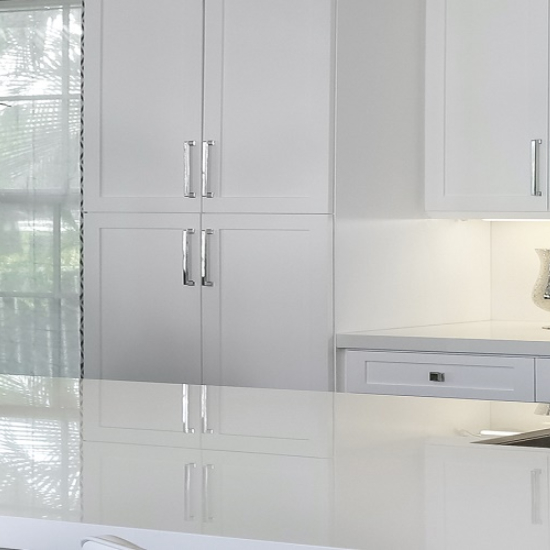 Encimera blanca Neolith Arctic White en cocina con gabinetes blancos y ventana luminosa.