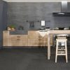 Cocina con encimera Neolith Aspen Grey gris, gabinetes madera, fregadero y taburete en suelo negro.