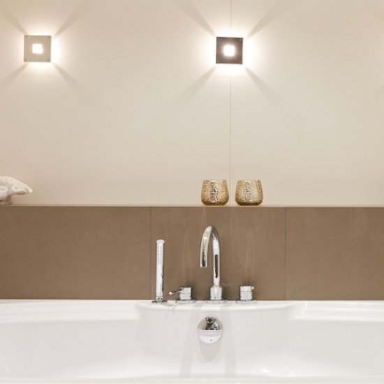 Bañera blanca con revestimiento Neolith Barro terracota, grifo plateado y velas doradas en baño minimalista.