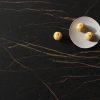 Superficie Neolith Mamba Málaga con frutas y vajilla, textura negra con vetas doradas luminosas.