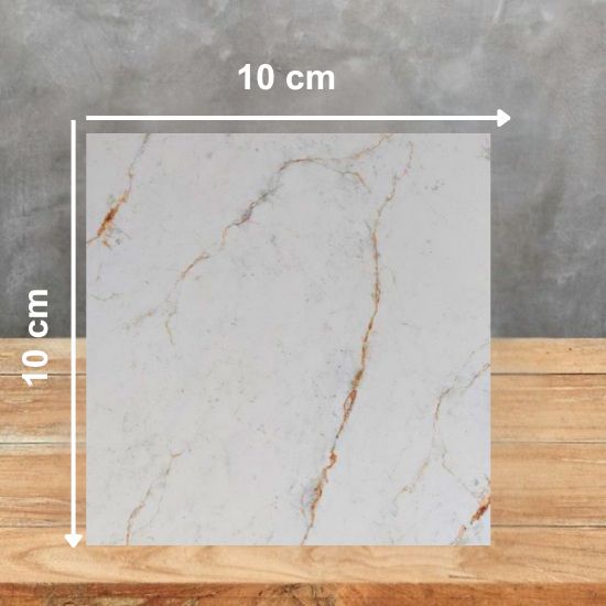 Muestra 10 × 10 cm de encimera Blaker Alhambra Gold sobre madera, mostrando el color blanco y vetas doradas reales.