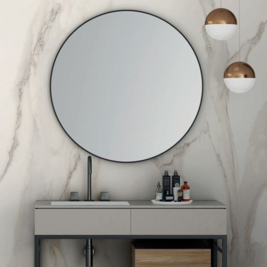 Vanitorio Blaker Toscana Gold blanca veteada con espejo redondo, grifo negro y productos en baño elegante.