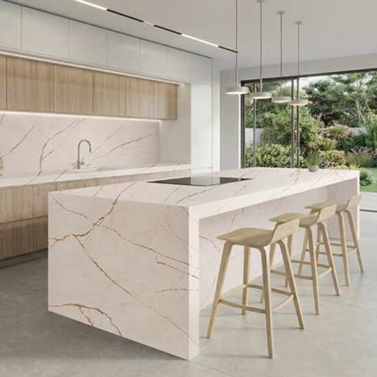 Cocina moderna con isla Ceratop Macadamia Cream crema veteado, gabinetes blancos, luces lineales y vista ventana en ambiente luminoso.