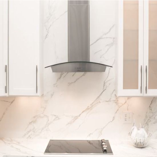 Encimera y salpicadero Blaker Calacatta Sun blanca veteada con campana plateada y gabinetes blancos en cocina luminosa.