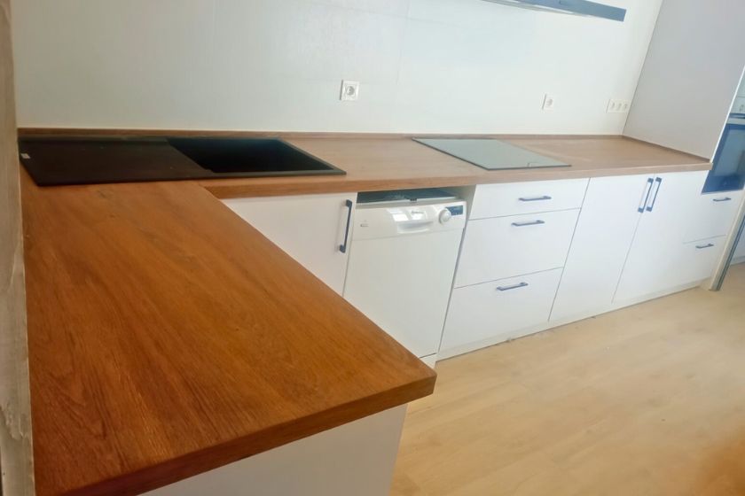 Instalación profesional de encimera porcelánica efecto madera SapienStone Rovere Baio en cocina de Puerto de la Torre Málaga 2025 con isla en L, encastre de vitrocerámica y horno. Tonos roble medio cálidos y textura natural realista.