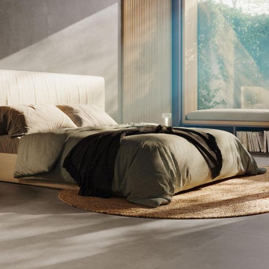 Dormitorio minimalista con piso Venux Bellissima Grigio veteado, cama blanca, manta gris y alfombra redonda en ambiente luminoso con vista natural.