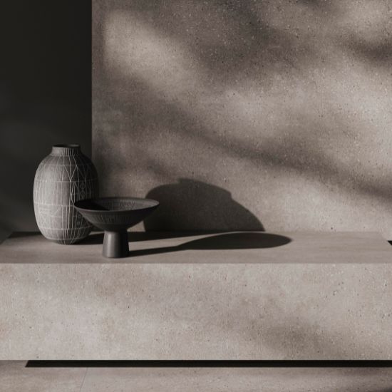 Baño moderno con encimera de baño Venux Bellissima Grigio gris veteado, espejo redondo, grifo bronce y productos en ambiente cálido.