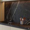 Cocina moderna con encimera y salpicadero Venux Calacatta Black negra veteada, grifo plateado y utensilios en ambiente elegante.
