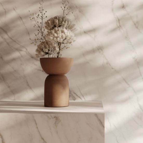 Baño moderno con encimera de baño Venux Calacatta Classic blanca veteada, espejo redondo, grifo dorado y toalla en ambiente cálido.