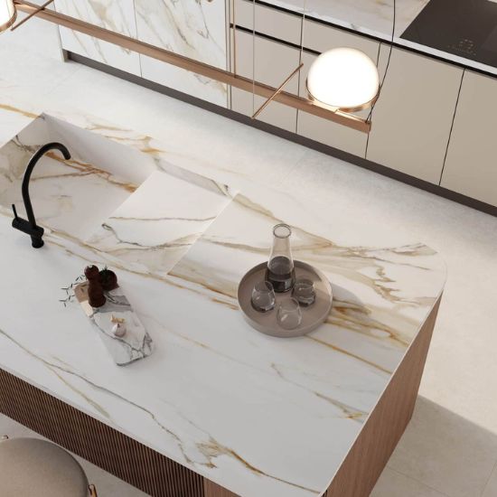 Cocina moderna con isla Venux Calacatta Gold blanca veteado, taburetes madera y gabinetes oscuros en ambiente elegante con vista jardín.