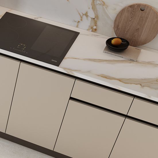 Vista cercana de encimera Venux Calacatta Gold blanca veteada con tabla de cortar, limón y libro en cocina moderna.