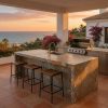 Isla de cocina exterior en Pizarra Multicolor con taburetes y barbacoa al atardecer