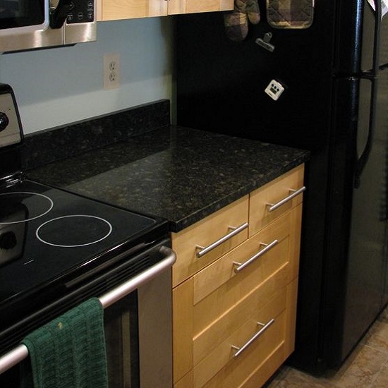 Encimera de Granito Steel Gray con vitrocerámica en cocina con muebles de madera clara