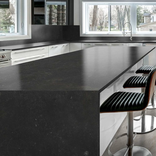 Isla de cocina en porcelánico Techlam Pierre Bleue negro con taburetes y muebles blancos