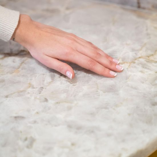 Mano sobre superficie cuarcita Terra Polaris mostrando textura suave y luminosa