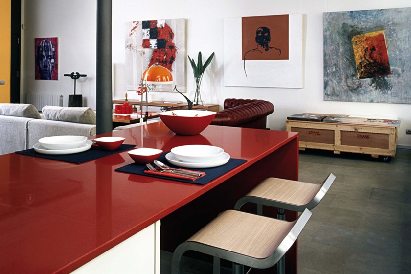 Bold red quartz kitchen island in modern open-plan living space with contemporary art
