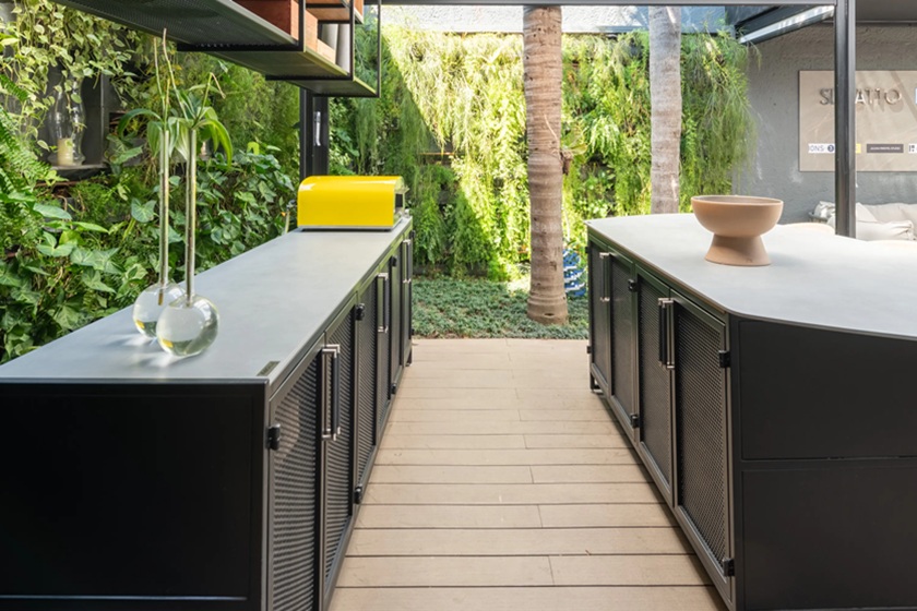 Modern outdoor kitchen with beige countertop and black cabinetry in a garden setting